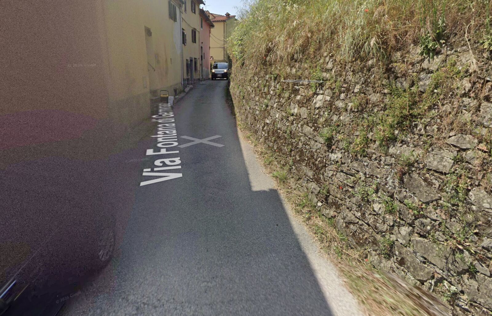 Via Fontana di Germinaia: a sinistra le facciate delle case sulla strada, a destra un alto muro a secco in pietra coperto d'erba; un furgone occupa tutta la carreggiata.